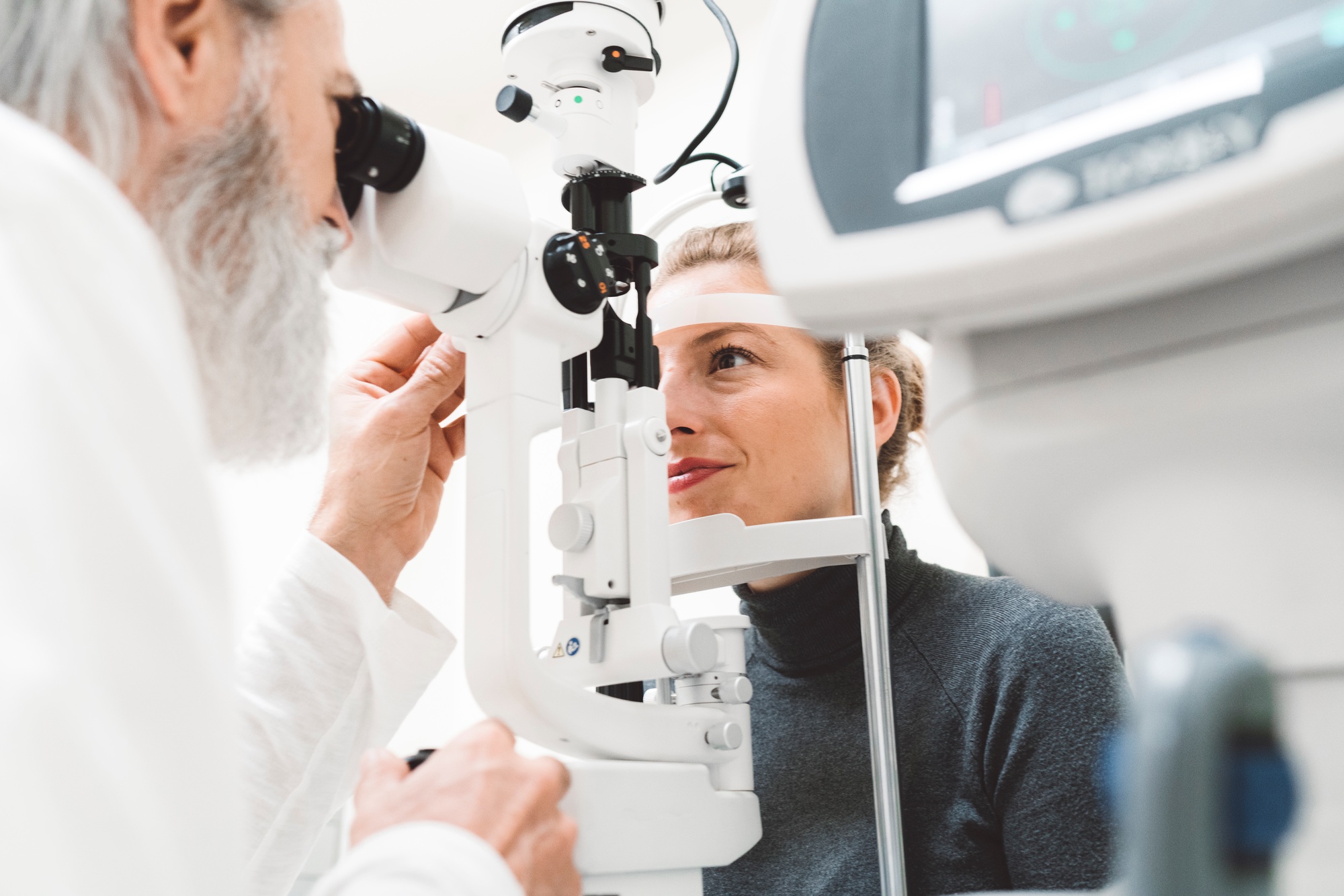 Senior ophthalmologist checking eyesight of a young smiling woman. Patient at doctor for eye examina